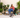 A woman in a red hoodie holds a potted plant, sitting among lush greenery with a Husky lying at her feet.