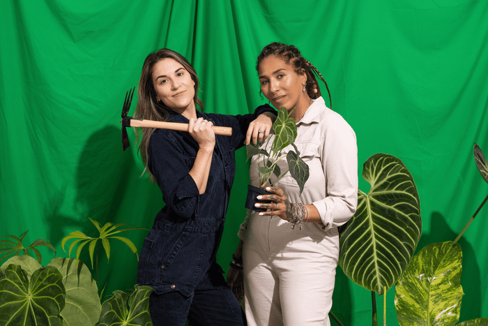 two women surrounded by plants, holding a pick and an Anthurium