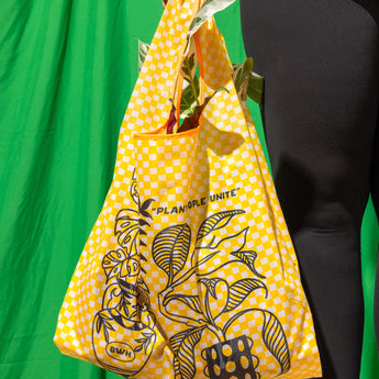 A person holding a yellow checkered reusable bag with plant illustrations and text on it.
