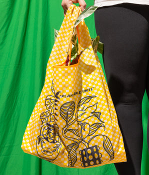 A person holding a yellow checkered reusable bag with plant illustrations and text on it.