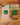 A set of stickers featuring the text 'FRAGILE AF' in green, yellow, and black, displayed on a wooden surface next to a clear plastic bag containing a green skull sticker.